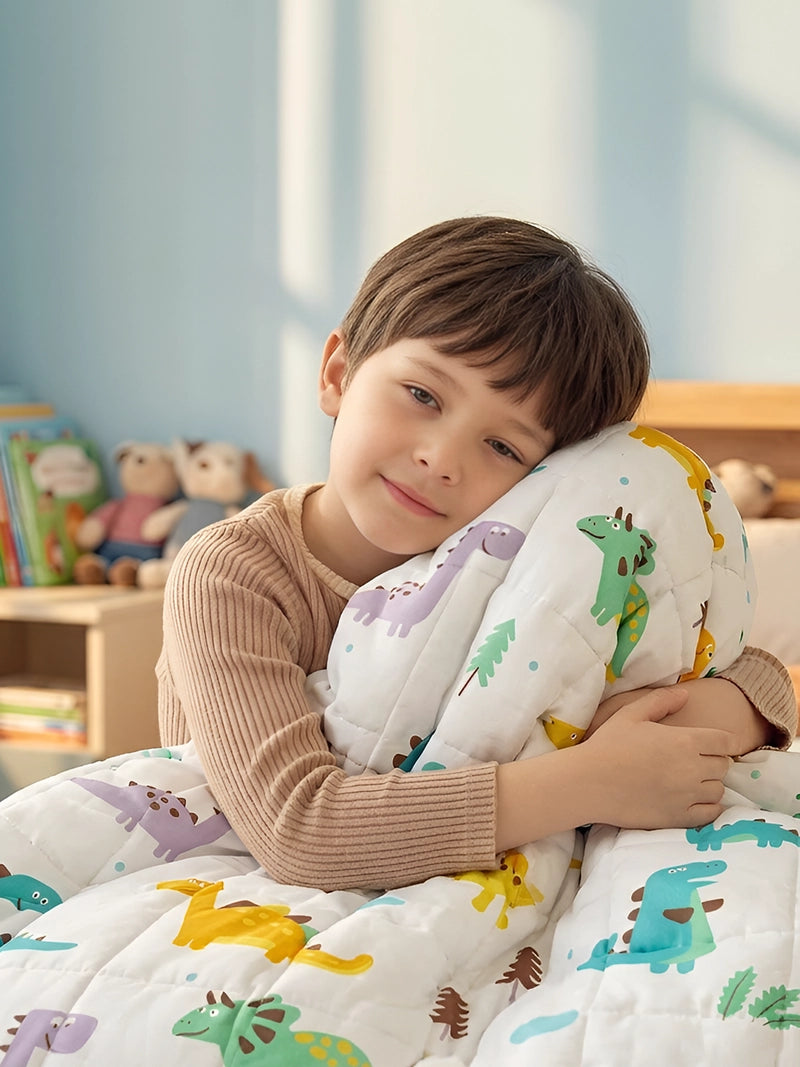 Lachende jongen knuffelt zittend een kinderverzwaringsdeken met dinoprint.